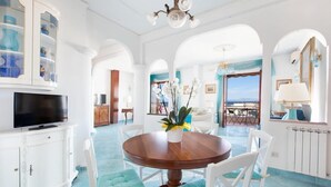 A spacious dining area with a round table, white chairs, and a television on a cabinet. - Casa Duca, apartment with sea views in Sorrento (Meta di Sorrento)