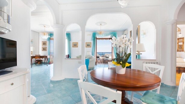 A spacious dining area with a round wooden table, white chairs, and a vase of flowers. - Casa Duca, apartment with sea views in Sorrento (Meta di Sorrento)