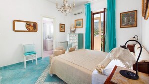 A bedroom with a bed, a chair, a dresser, a chandelier, and a view through a door. - Casa Duca, apartment with sea views in Sorrento (Meta di Sorrento)