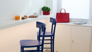 A dining area with two blue chairs, a red handbag, a plant, and a glass of orange juice on a white shelf.