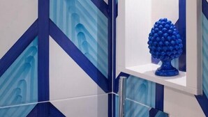 A bathroom with a geometric tile pattern, a shower, and a blue decorative item on a shelf.