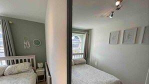 A bedroom with two single beds, a bedside table, a radiator, a dreamcatcher, a clock, and framed pictures on the wall. - Lancaster 1 bed Cottage Apartment- M6 - Lancs Uni (Lancaster)