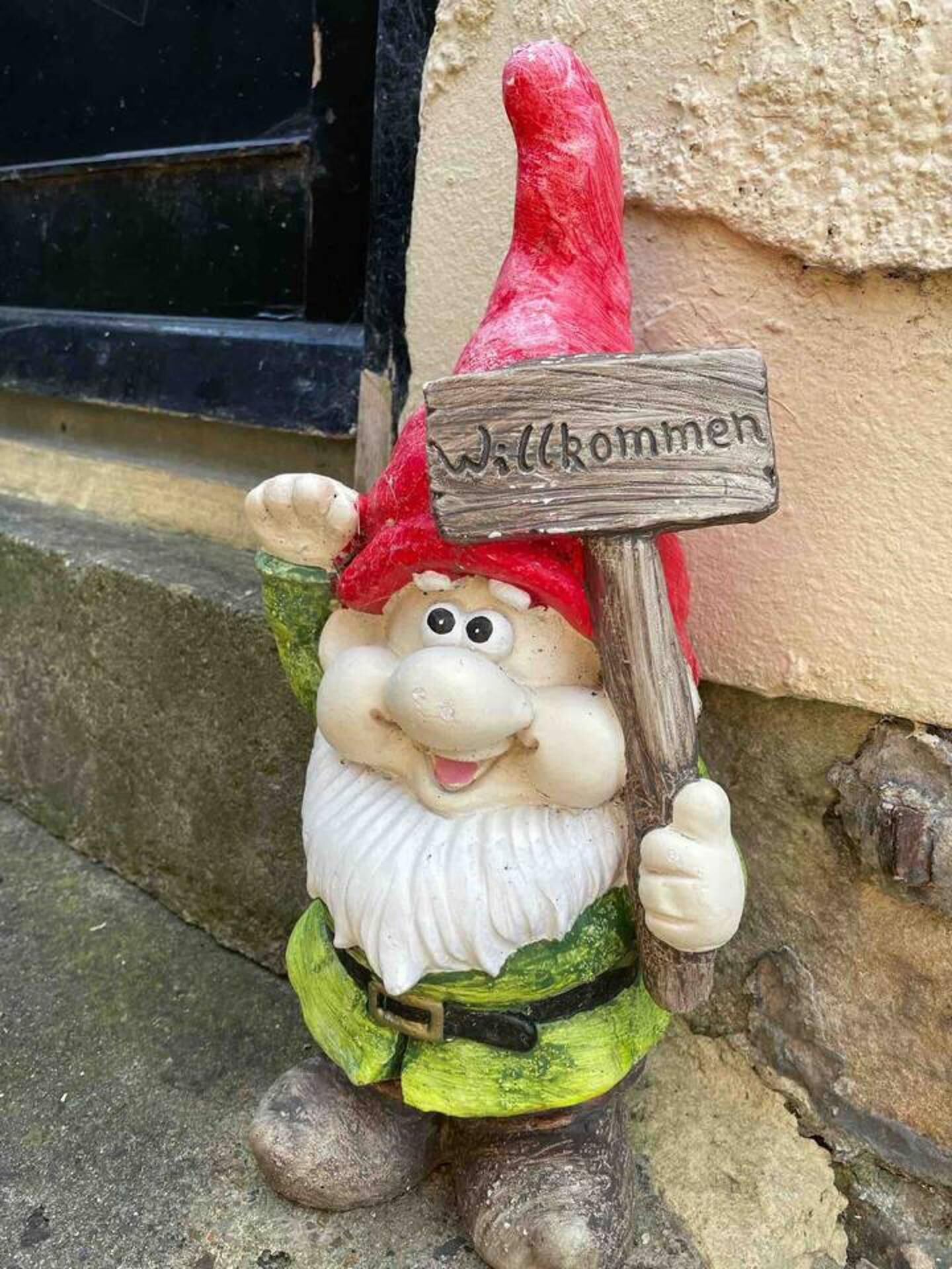 A garden gnome holding a sign that says "Willkommen" (Welcome) in front of a building.