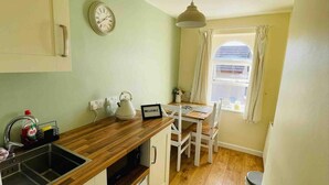 A small kitchen with a wooden countertop, a kettle, a clock, and a window with curtains. - Lancaster 1 bed Cottage Apartment- M6 - Lancs Uni (Lancaster)