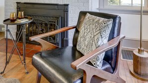 Un salón con chimenea, un sillón de cuero, una mesita con velas y una ventana con persianas.