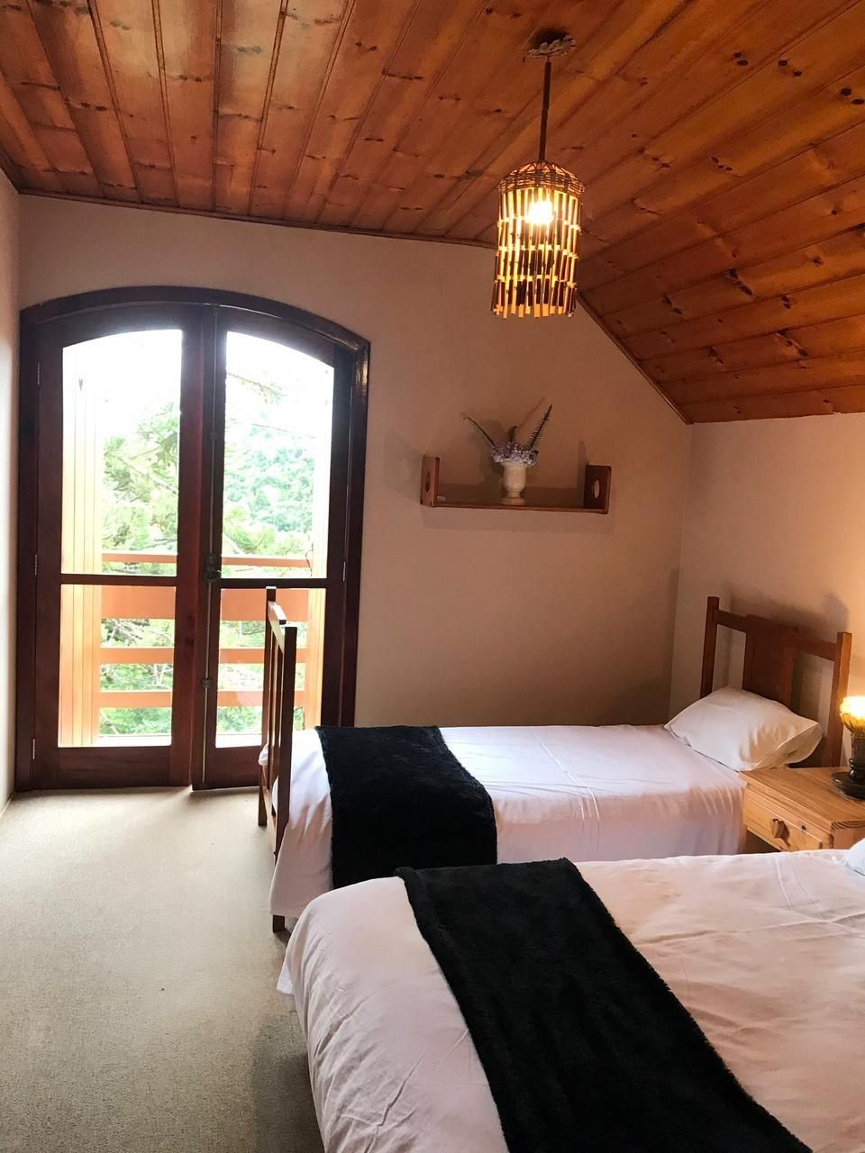 Un dormitorio con dos camas, techo de madera, un ventanal grande y una lámpara colgante.