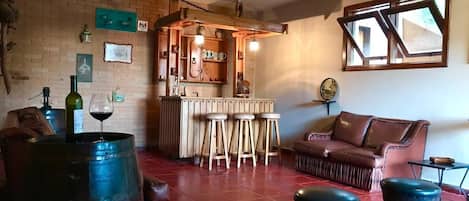 A cozy living room with a brick wall, a wooden bar area with stools, a leather sofa, and a large barrel.
