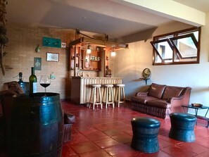 A cozy living room with a brick wall, a wooden bar area with stools, a leather sofa, and a large barrel. - Country Home (Campos do Jordão)
