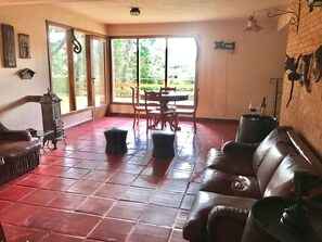 A spacious living room with a leather sofa, a dining table with chairs, and a large sliding glass door leading to a garden. - Country Home (Campos do Jordão)
