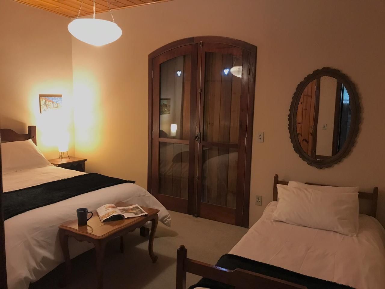 Habitación de hotel con dos camas, un armario de madera, una mesita de noche con un libro y una taza, y un espejo en la pared.