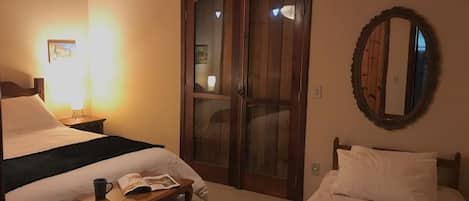 Habitación de hotel con dos camas, un armario de madera, una mesita de noche con un libro y una taza, y un espejo en la pared.