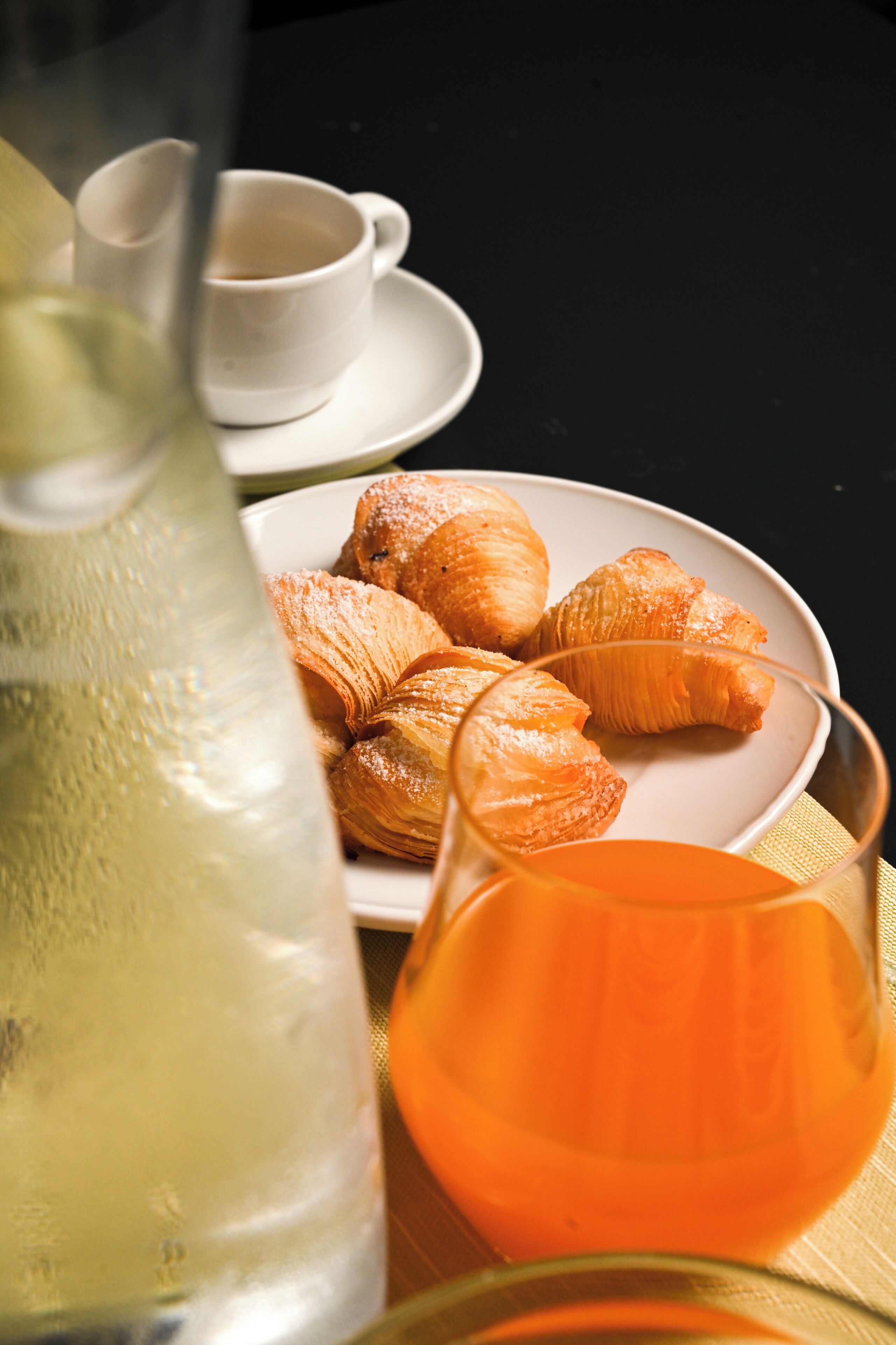 Ein Tisch mit einem Teller Croissants, einem Glas Orangensaft und einer Wasserflasche.