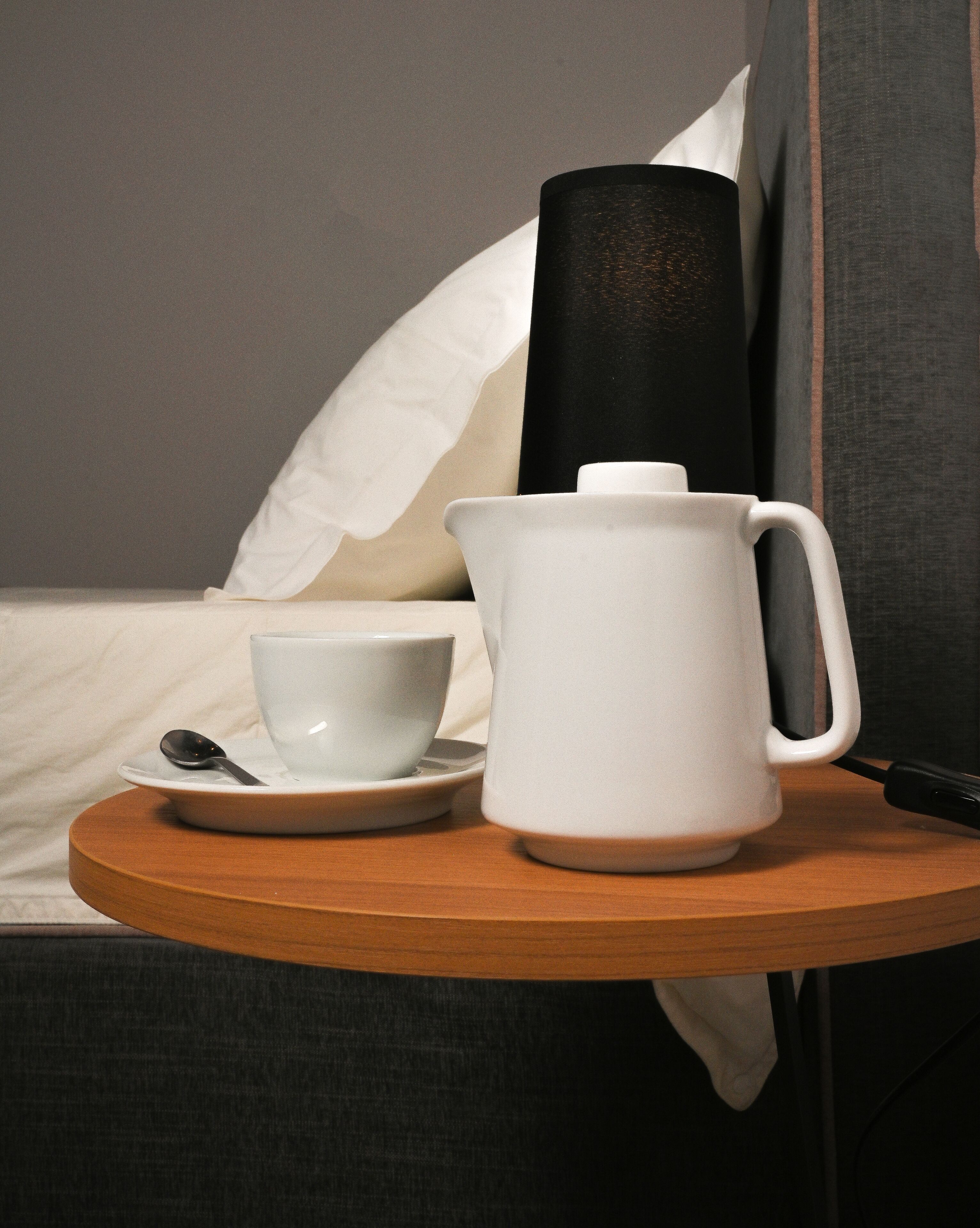 Una cafetera blanca, una taza blanca y una cuchara sobre una bandeja de madera.