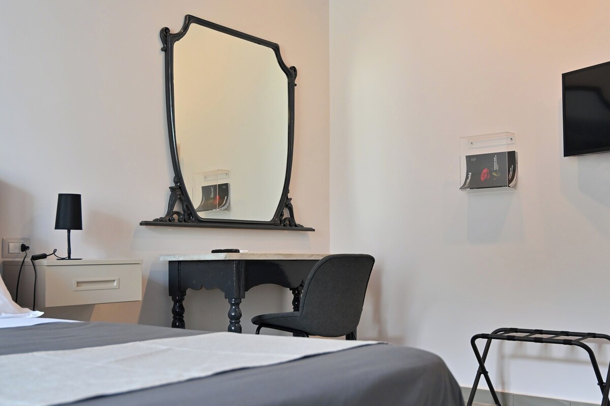 Une chambre d’hôtel comprenant un lit, un bureau, une chaise, un miroir, un téléviseur et un panneau de commande fixé au mur.