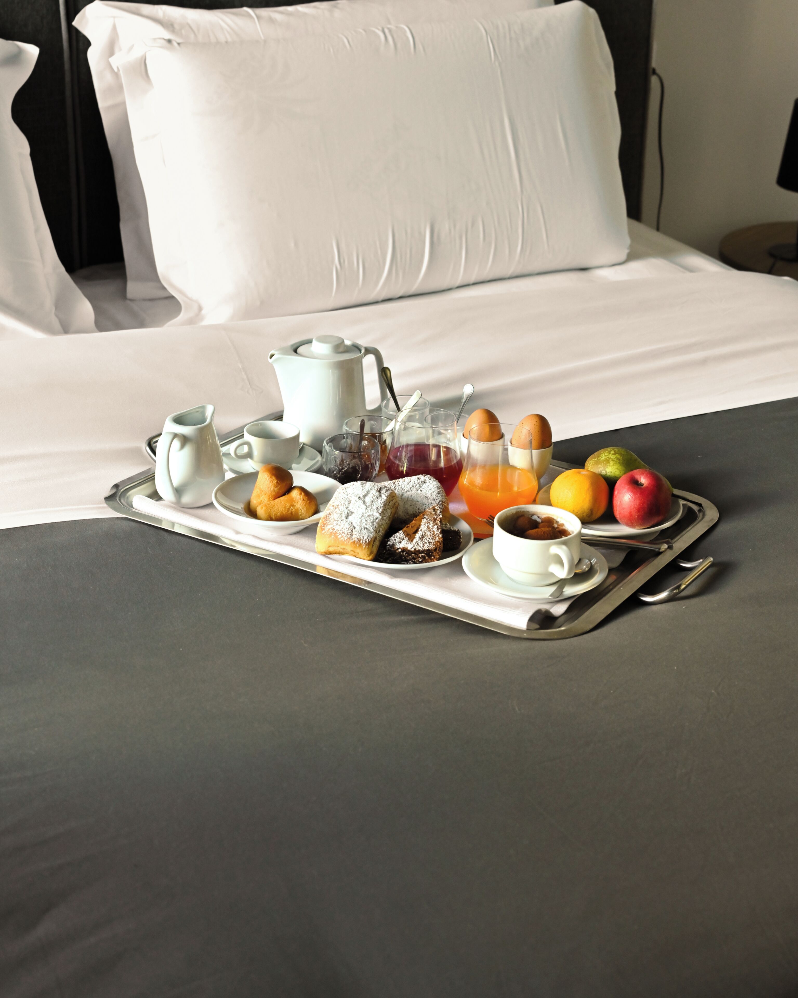 Una bandeja de desayuno ordenada sobre una cama, con un almohadón y un cabecero al fondo.