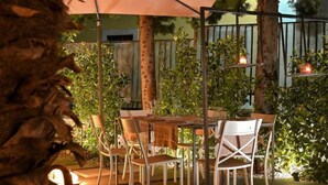 An outdoor patio with a table and chairs under a canopy, surrounded by trees and plants. - Ghe Kale' Resort (San Paolo Bel Sito)