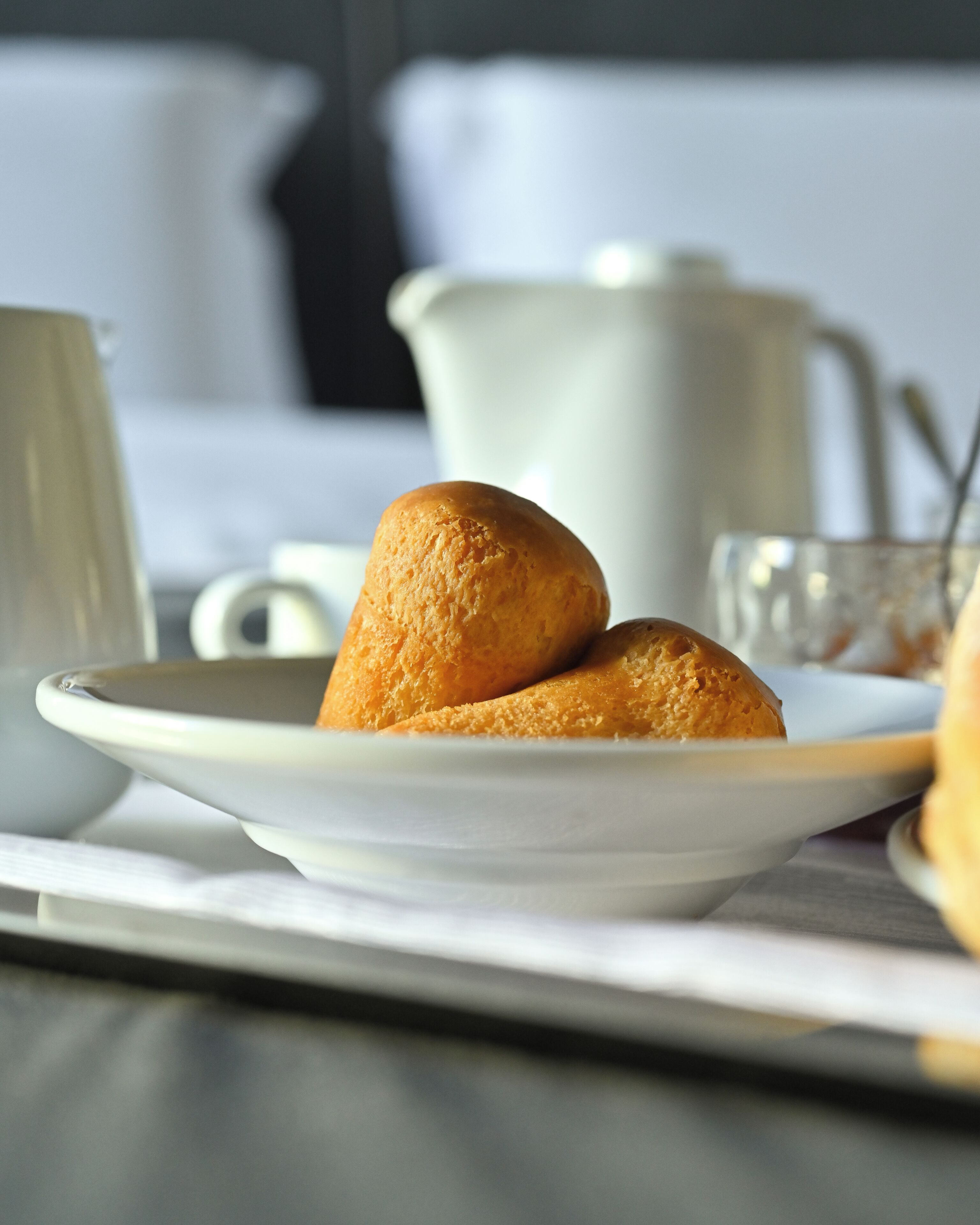 Un plat amb dues pastissos sobre una taula, una tassa blanca i una gerra blanca al fons.