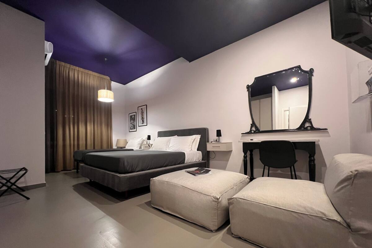 Ein Hotelzimmer mit einem Bett, einem Schreibtisch mit Spiegel, einem Sessel und einem kleinen Tisch.