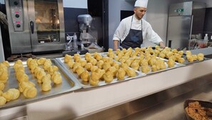 A commercial kitchen with a chef preparing food, multiple trays of pastries, and kitchen equipment. - Ghe Kale' Resort (San Paolo Bel Sito)