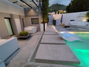 Ein moderner Außenbereich mit Terrasse, Pool, Sitzgelegenheiten und Blick auf einen Hügel.