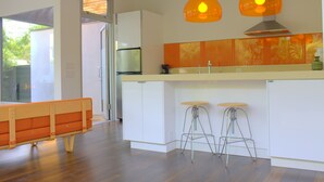 Una cocina moderna con armarios blancos, dos taburetes de bar e iluminación colgante.