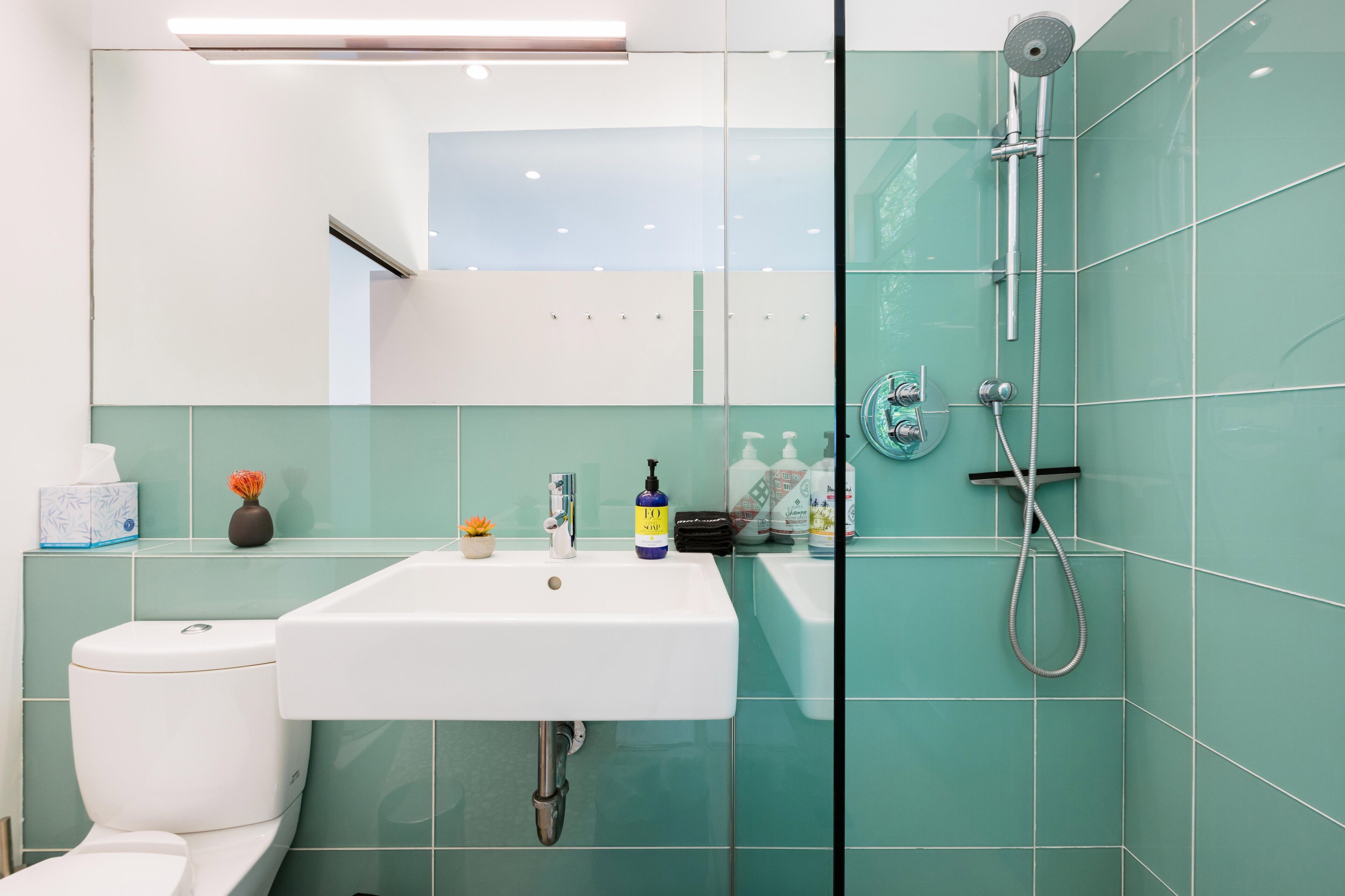Un baño moderno con un lavamanos blanco, un box de ducha con mampara de vidrio y azulejos color turquesa.
