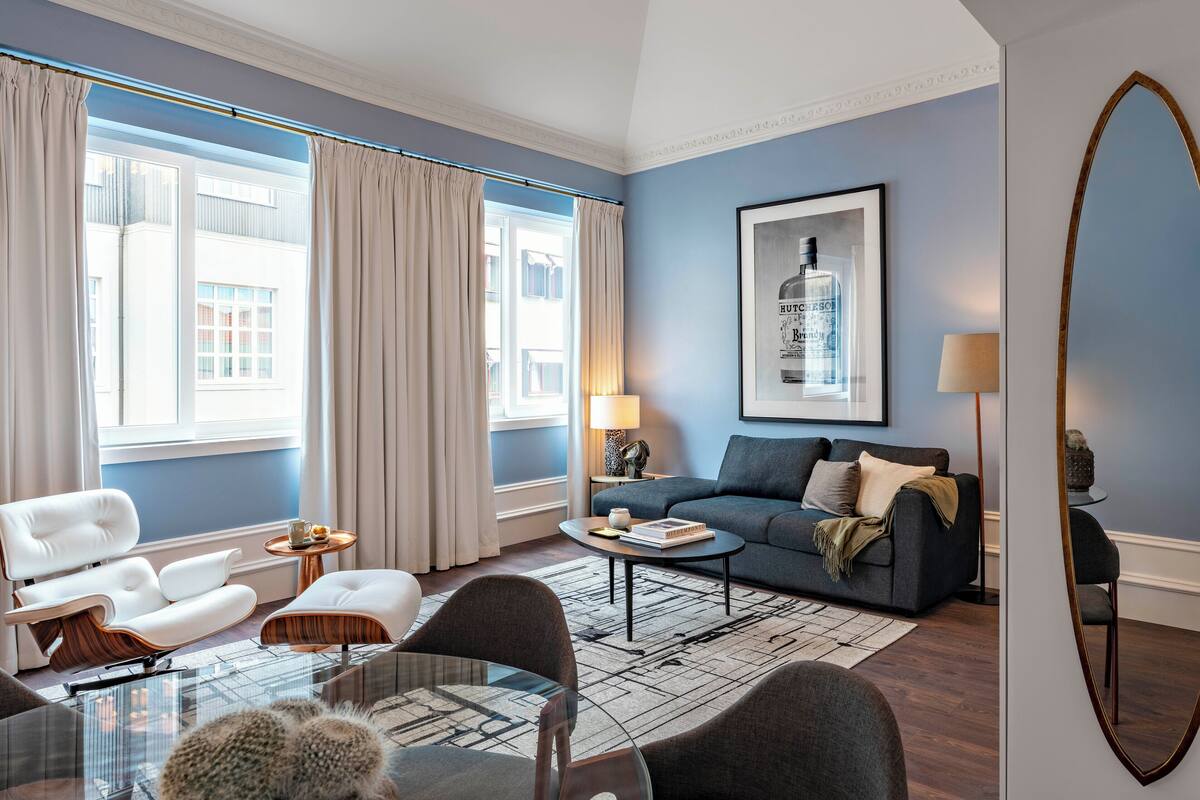 Una sala de estar moderna con una pared azul de acento, un ventanal con cortinas, un sofá, una mesa de centro y un comedor con sillas y una mesa de vidrio.