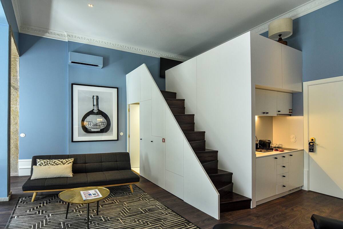 Un área de estar moderna con un sofá, una mesa de centro y una escalera que lleva a una cocina.