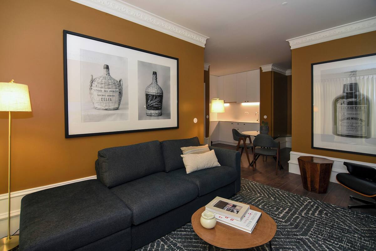 Una sala moderna con un sofá gris oscuro, una mesa redonda con libros y botellas de licor enmarcadas en la pared.