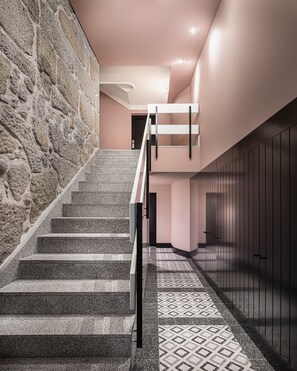 A staircase with a stone wall on one side and a patterned floor. - Almada 234 (Porto)