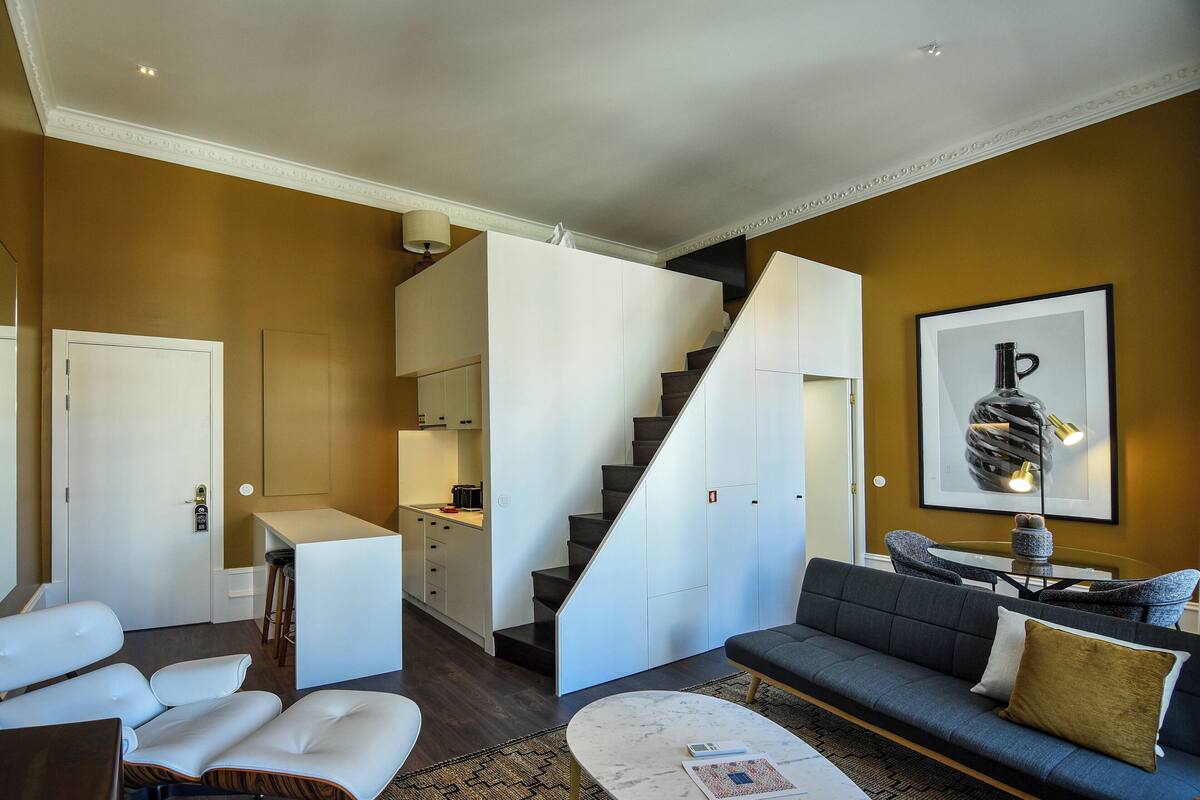 Una sala de estar moderna con un sofá, una mesa de centro y una escalera que lleva a una cocina.