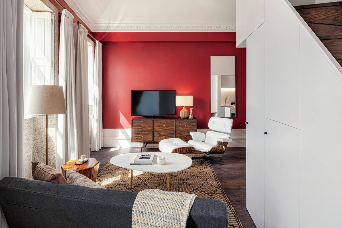 Una sala moderna con una pared de acento roja, un televisor de pantalla plana, un sofá blanco, una mesa de centro y una alfombra estampada.
