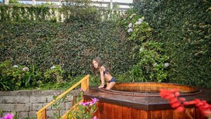 A wooden hot tub in a garden with a stone wall and wooden steps leading up to it. - Casa das Montanhas  (Campos do Jordão)