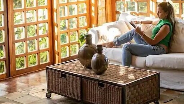 A room with a large window, a sofa, and a wicker coffee table. - Casa das Montanhas  (Campos do Jordão)