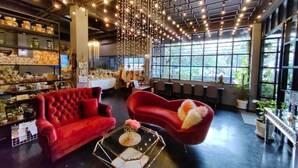 A spacious room with a red sofa, a red armchair, and a glass coffee table. There are shelves with various items and a large window providing natural light. - The Willow Phangan (Ko Pha-ngan)
