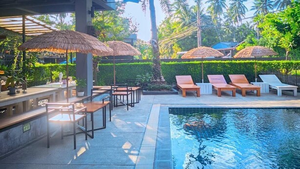 A poolside area with lounge chairs and umbrellas, surrounded by lush greenery and palm trees. - The Willow Phangan (Ko Pha-ngan)