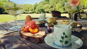 Uma disposição para piquenique com uma mesa de madeira, um copo de vinho branco, uma rosa em um copo, queijo e uma xícara com motivos florais.
