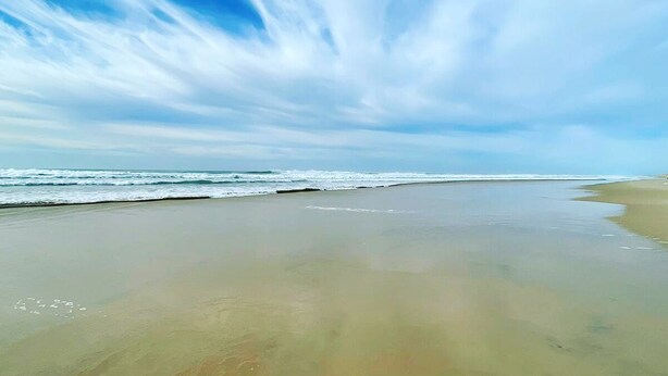 Uma praia com extensa faixa de areia e ondas suaves.