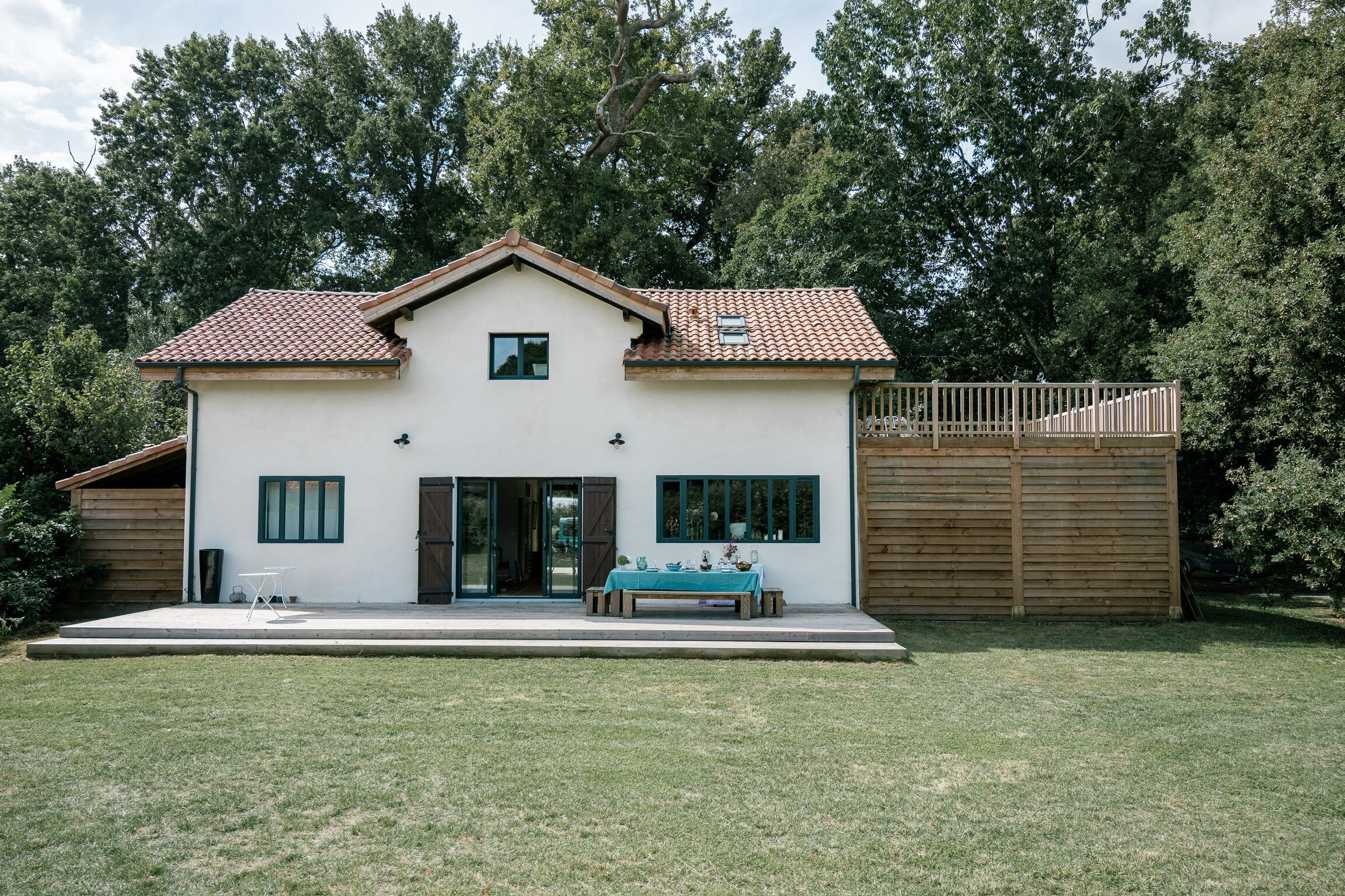 A two-story house with a tiled roof, a front porch, and a wooden fence.