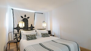 Um quarto bem arrumado com uma cama, duas mesas de cabeceira, duas luminárias fixadas na parede e uma tapeçaria decorativa.