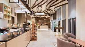 A modern hotel lobby with a central reception desk, a long counter with seating, and a decorative ceiling. - Intercityhotel Bawshar Muscat (Muscat)