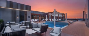 A rooftop pool area with lounge chairs and tables, a clear view of the sunset, and a modern building design. - Intercityhotel Bawshar Muscat (Muscat)