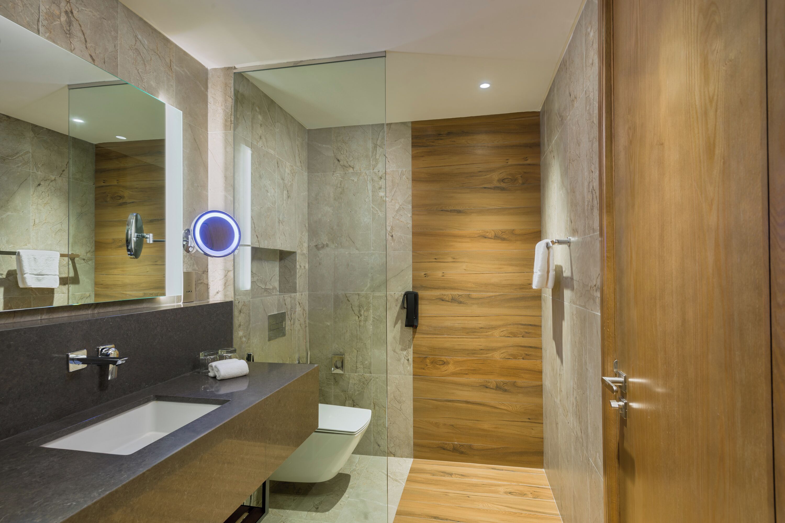 A modern bathroom with a marble sink, a toilet, and a wooden vanity.