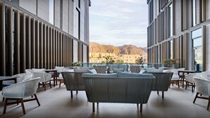 A modern indoor space with seating and tables, large windows, and a view of distant buildings and mountains. - Intercityhotel Bawshar Muscat (Muscat)