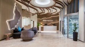 A modern hotel lobby with a reception desk, seating area, and a glass wall with a cityscape view. - Intercityhotel Bawshar Muscat (Muscat)