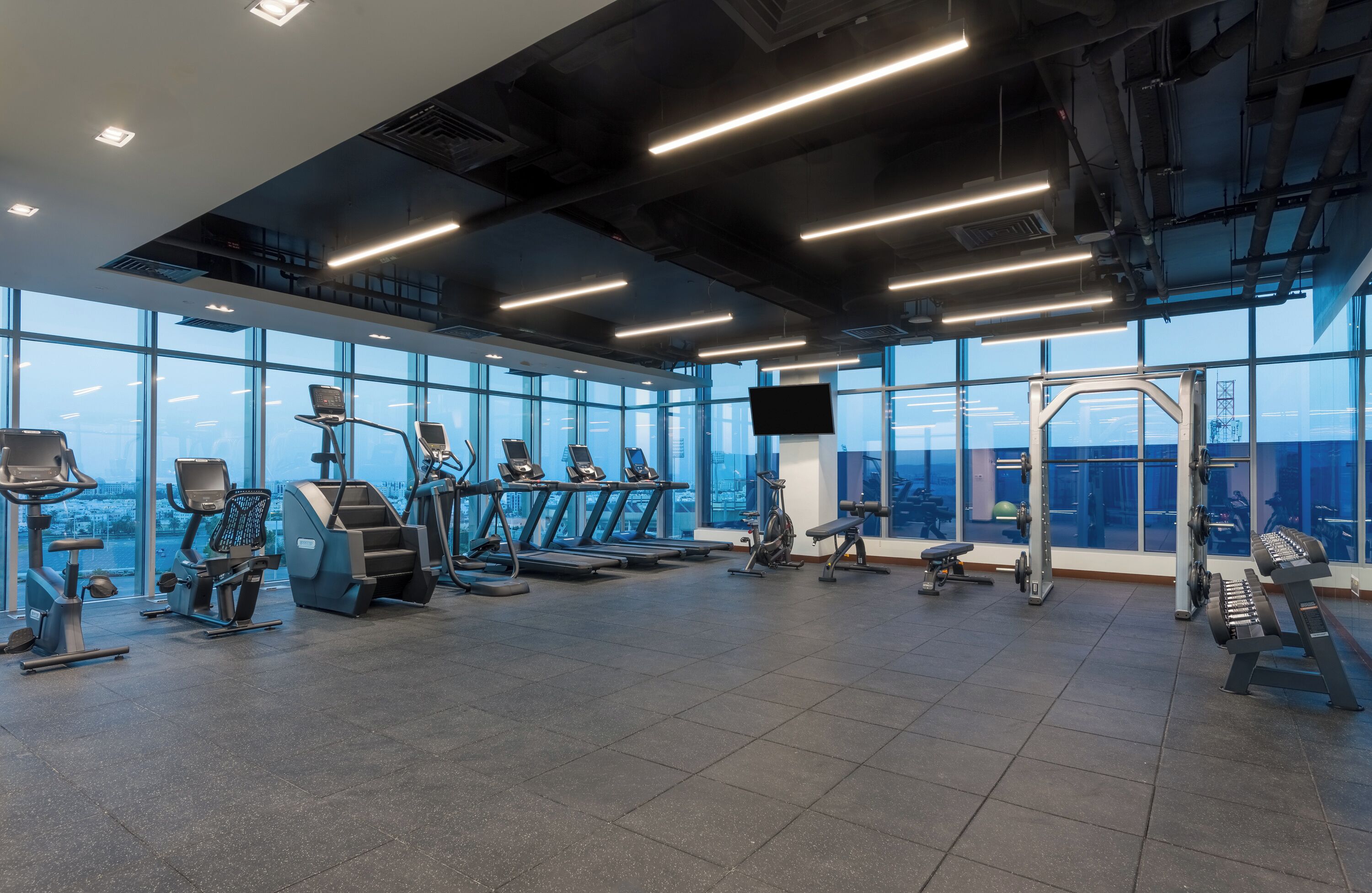 Een moderne sportschool met diverse trainingsapparaten, grote ramen en een stadsgezicht.