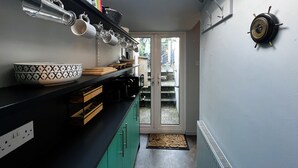 Una cocina con tragaluz, una estantería con libros, un colgador para ollas y una decoración de pared con temática náutica.