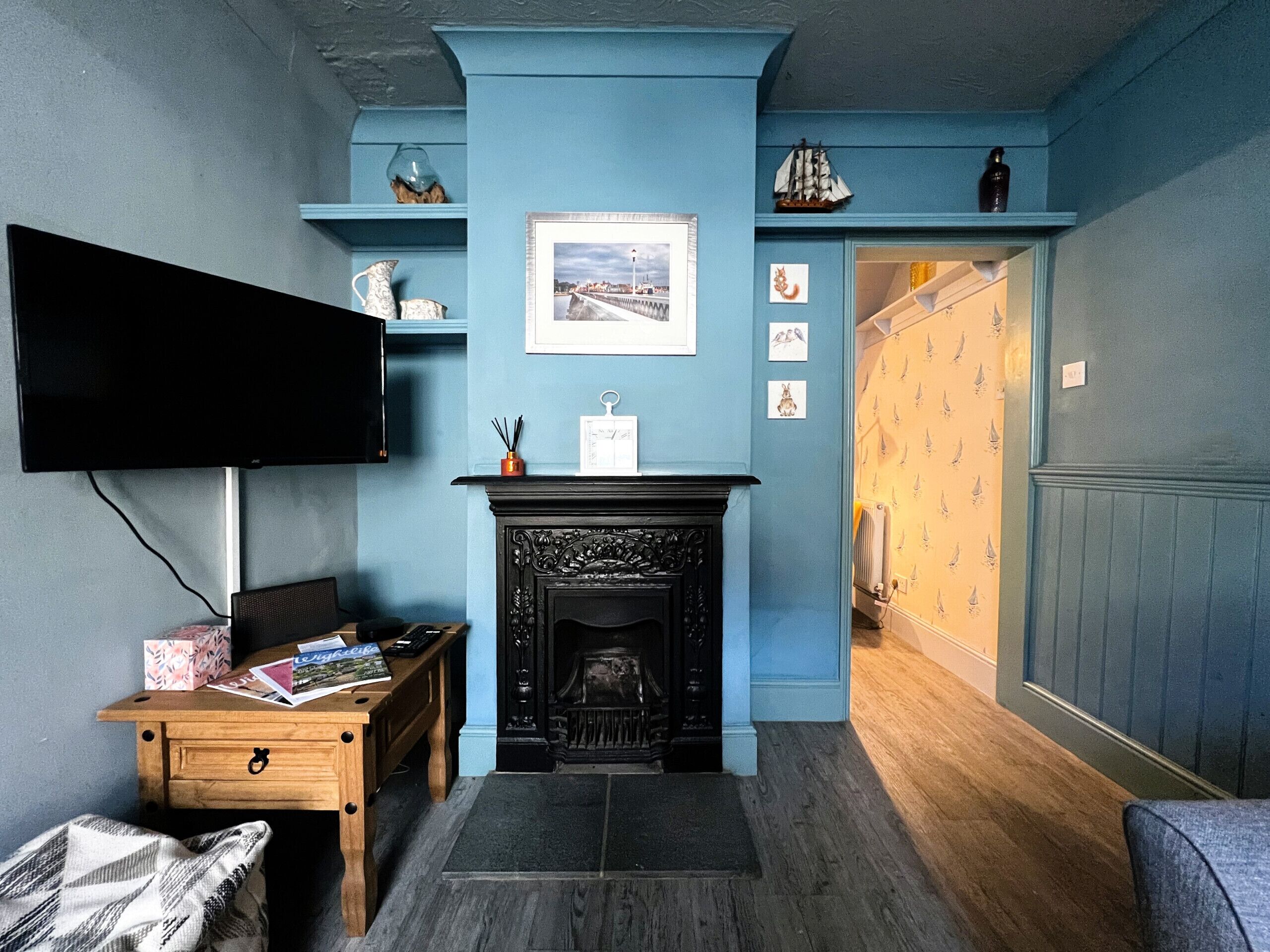 A room with a fireplace, a television mounted on the wall, a wooden bench, and a door leading to another room.