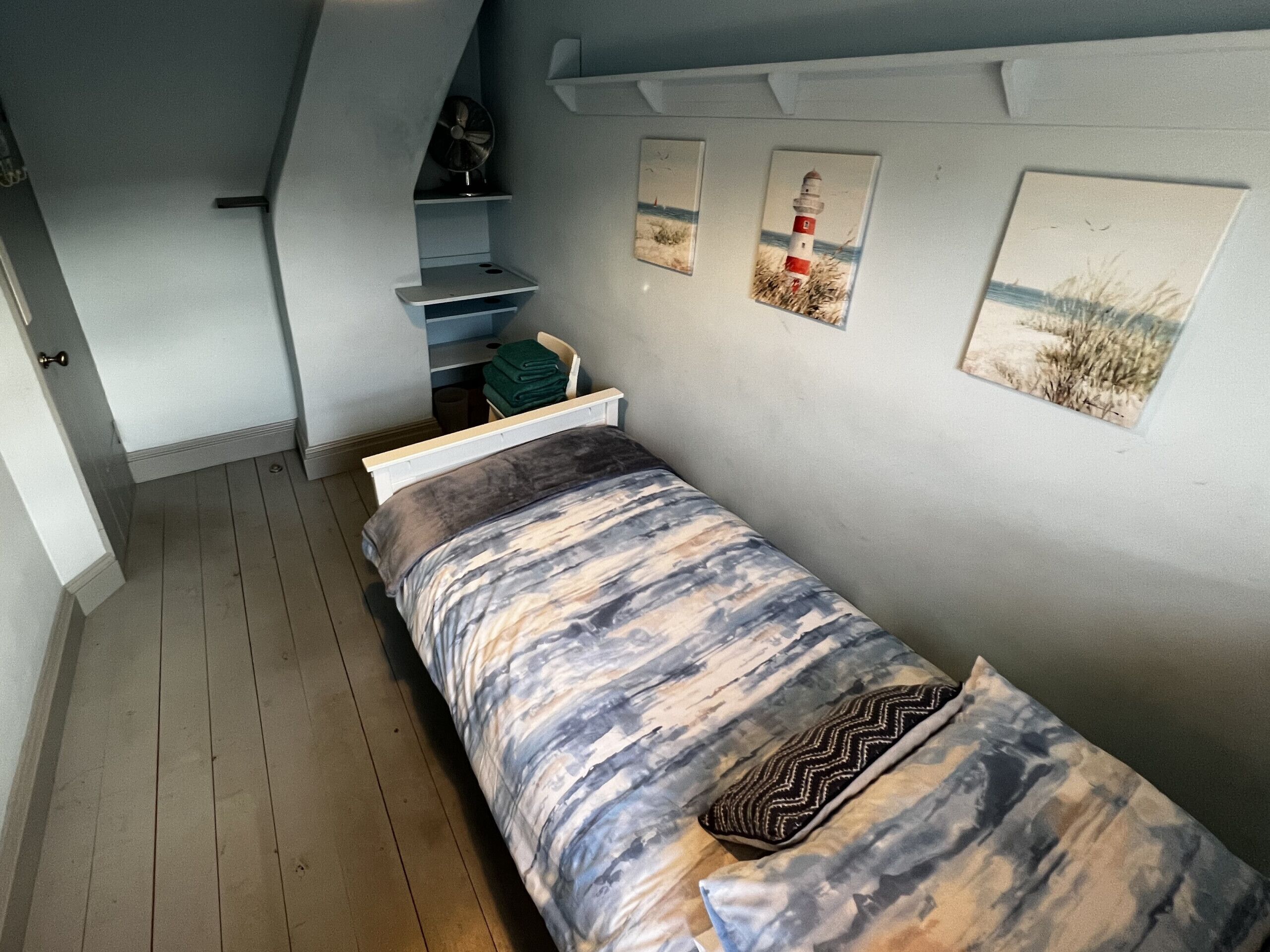 A bedroom with a bed, a small shelf, and three framed pictures on the wall.