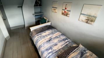 A bedroom with a bed, a small shelf, and three framed pictures on the wall.